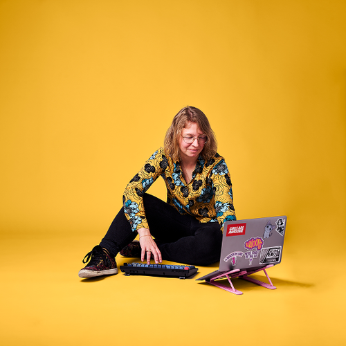 Louise sitting with a computer with a yellow background